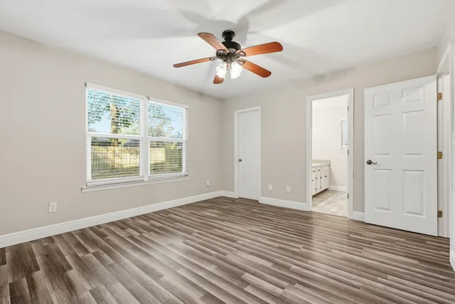 a view of an empty room with wooden floor and a ceiling fan