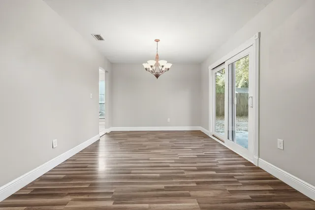 a view of empty room with wooden floor chandelier and window