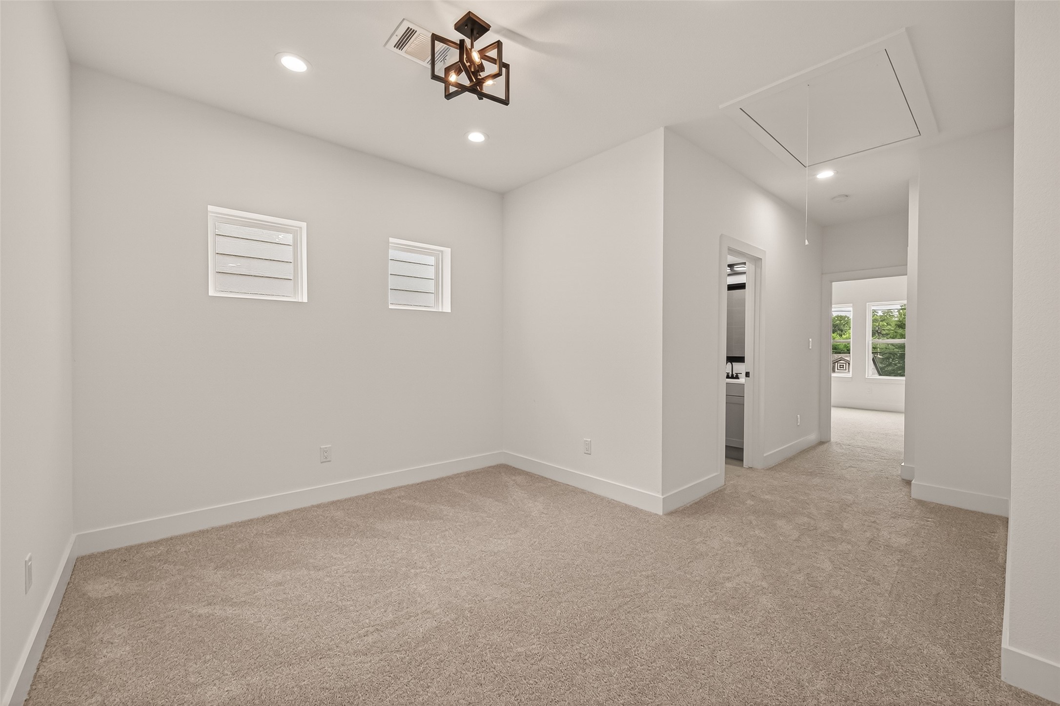 6808 Madrid Street Houston, TX 77021 - Photo 18 of 31 This photo shows a bright, carpeted room with modern lighting, featuring two small windows. The room leads to a hallway and has an adjacent space visible, suggesting an open layout.