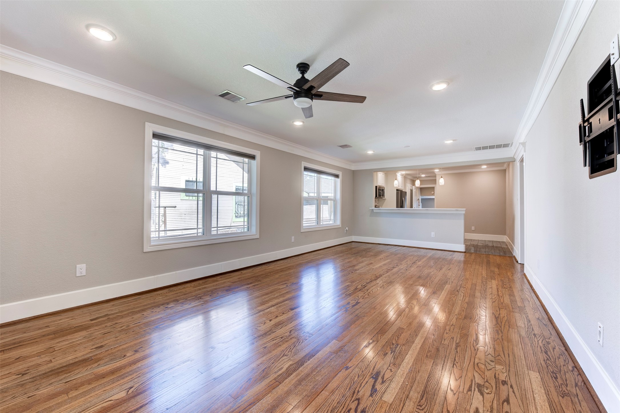 109 Dresden Street Houston, TX 77012 - Photo 4 of 43 This photo shows a spacious, open-concept living area with hardwood floors, neutral walls, and large windows for natural light. The room features recessed lighting, a ceiling fan, and a view into a modern kitchen with a breakfast bar.