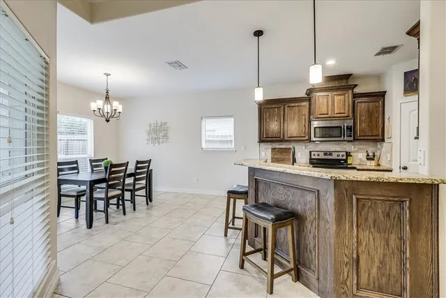 a kitchen with stainless steel appliances granite countertop a stove top oven a sink a dining table and chairs with wooden floor