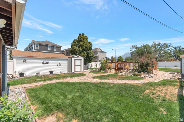 7391 Elm Street Midvale, UT 84047 - Photo 31 of 38 Expansive backyard featuring a manicured lawn, flagstone pathways, a wood deck, a storage shed, and a detached garage with horizontal siding