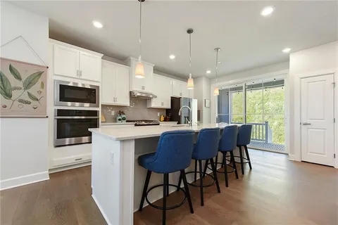 a kitchen with stainless steel appliances granite countertop a stove a refrigerator a kitchen island a dining table and chairs with wooden floor