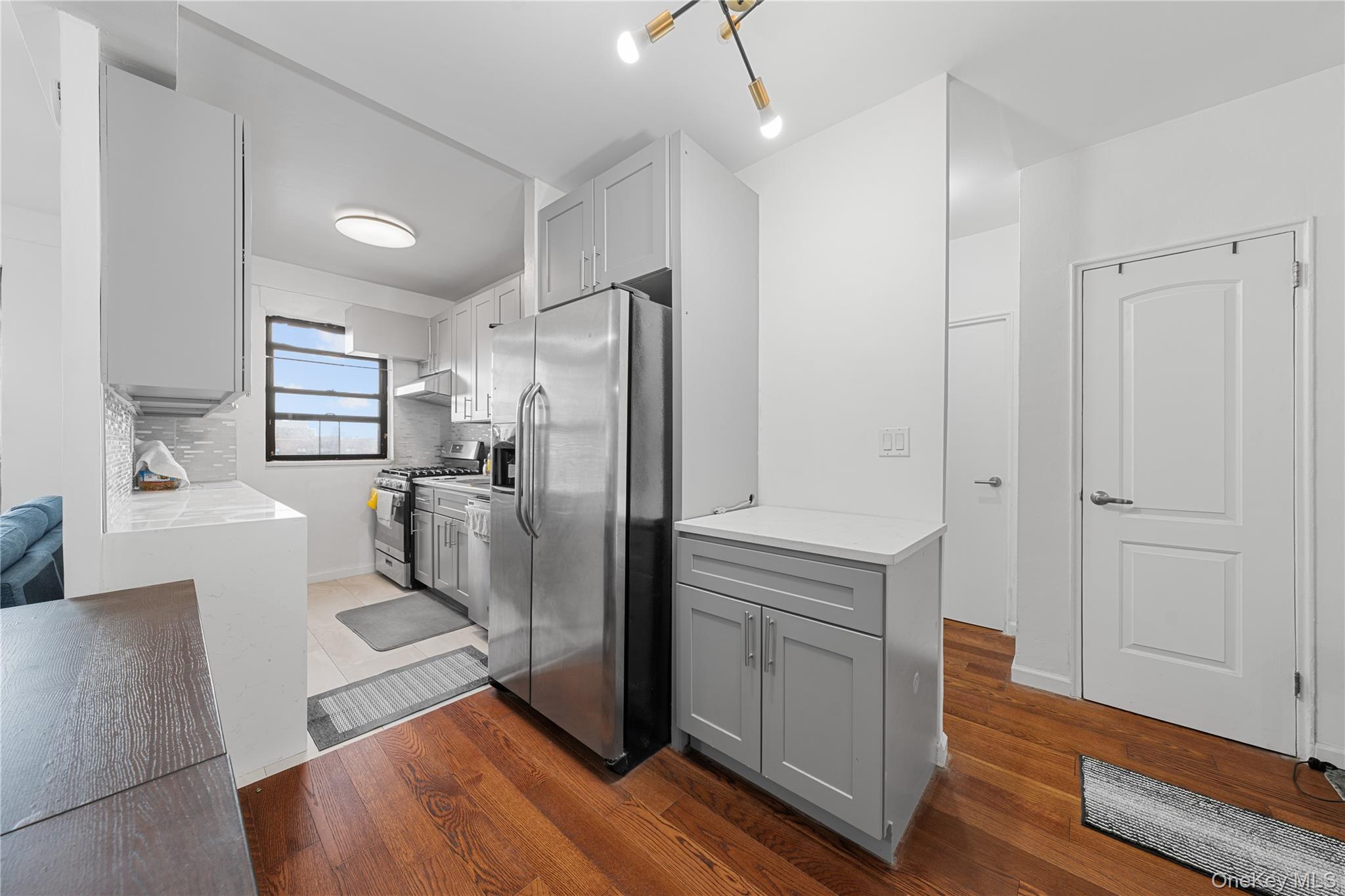 99-32 66th Road, Unit 5K Queens, NY 11374 - Photo 11 of 20 Kitchen with gray cabinetry, stainless steel appliances, light stone counters, and dark wood-style floors