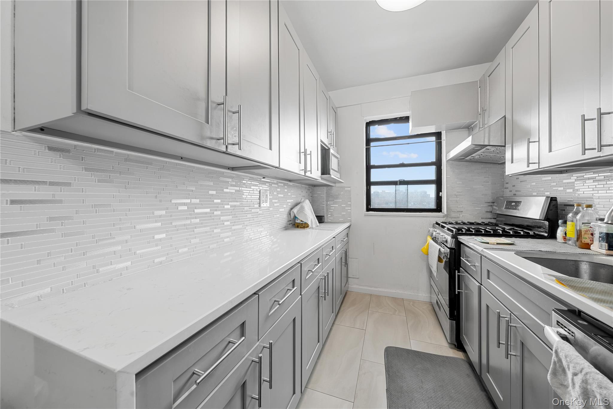 99-32 66th Road, Unit 5K Queens, NY 11374 - Photo 12 of 20 Kitchen with stainless steel appliances, gray cabinets, under cabinet range hood, light stone countertops, and light tile patterned floors