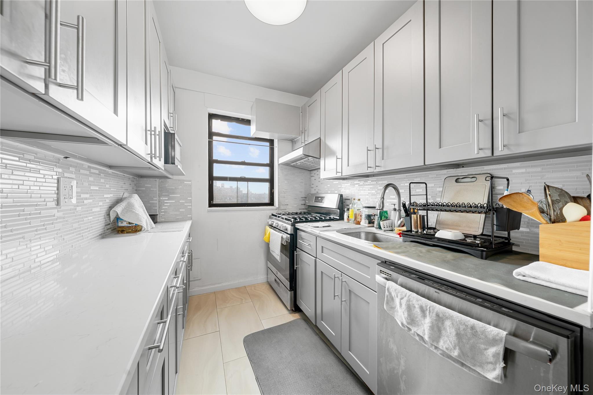 99-32 66th Road, Unit 5K Queens, NY 11374 - Photo 13 of 20 Kitchen featuring stainless steel appliances, decorative backsplash, under cabinet range hood, gray cabinets, and light stone countertops