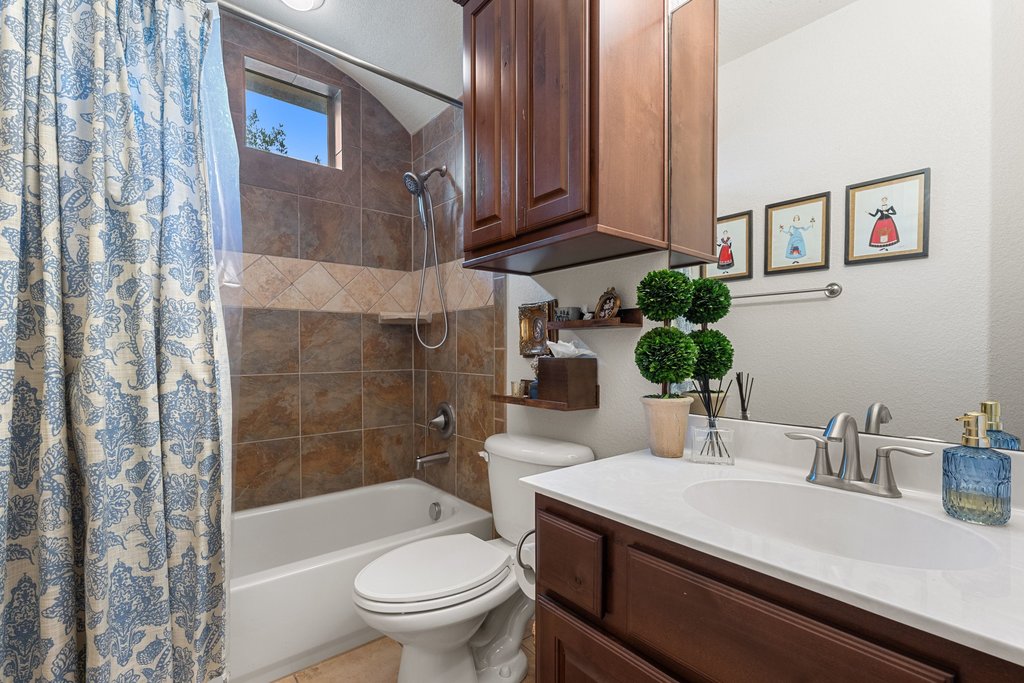 6708 Menchaca Road, Unit 2 Austin, TX 78745 - Photo 17 of 30 Full bathroom featuring a white tub with a tiled shower surround, an arched window, a toilet, a vanity with a white countertop and dark wood cabinetry, and a mirrored wall