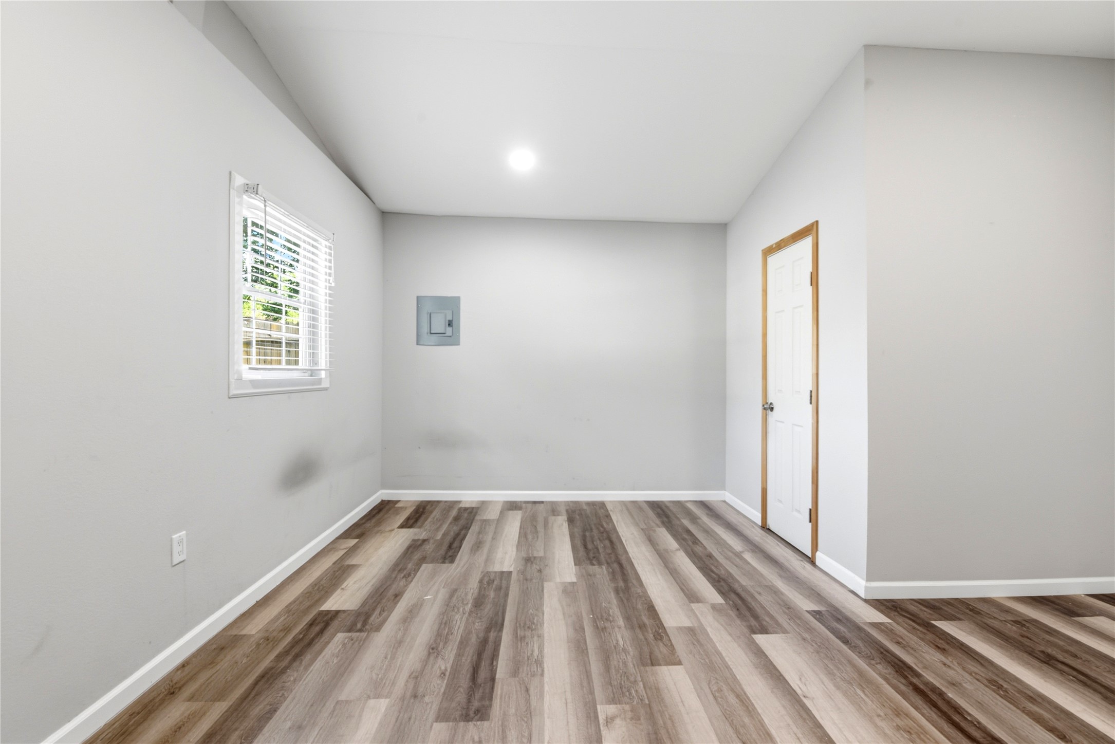 9403 Spaulding Street Houston, TX 77016 - Photo 42 of 50 This room features light gray walls, a window with blinds, and wood-look flooring. It has a door in the corner and a small wall fixture, providing a clean and neutral space ready for customization.
