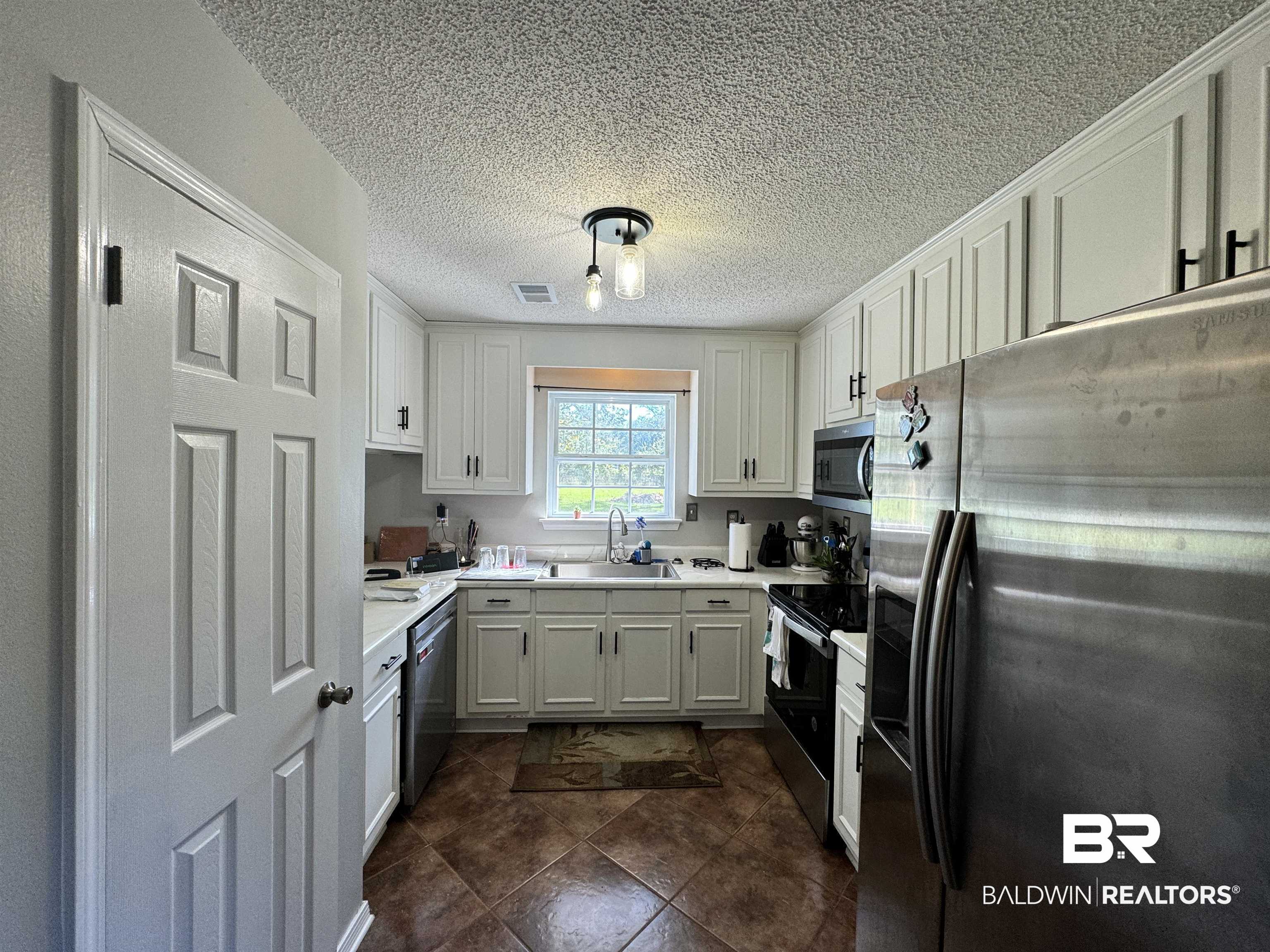 14313 Hemley Road Coden, AL 36523 - Photo 9 of 44 Kitchen with white cabinetry, a textured ceiling, dark tile patterned floors, sink, and stainless steel appliances