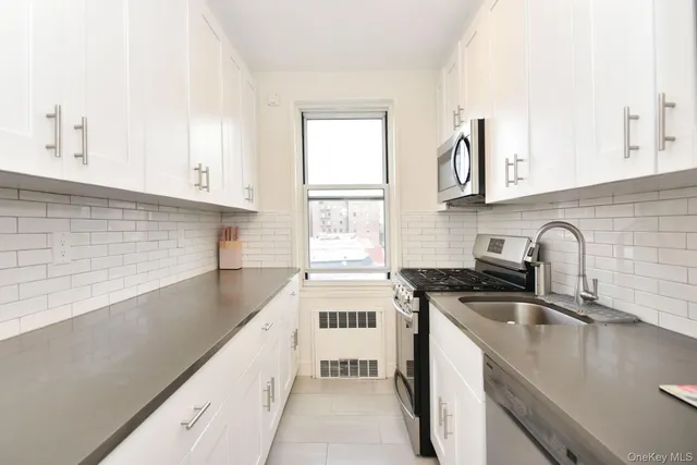 a kitchen with stainless steel appliances a sink a stove a sink a window and white cabinets