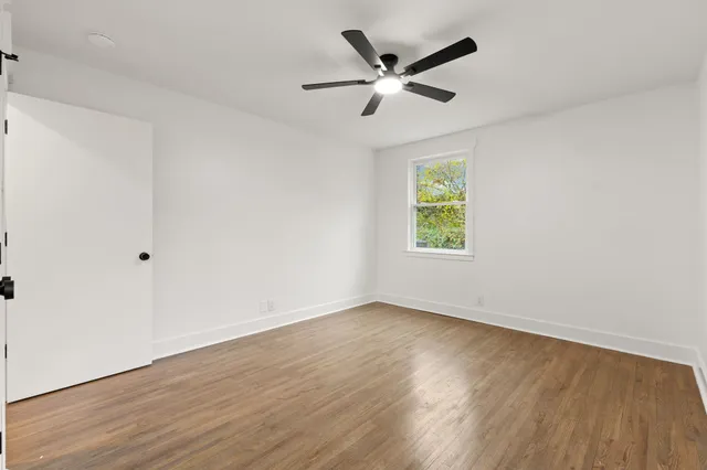 an empty room with wooden floor window and ceiling fan