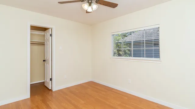 an empty room with wooden floor fan and windows