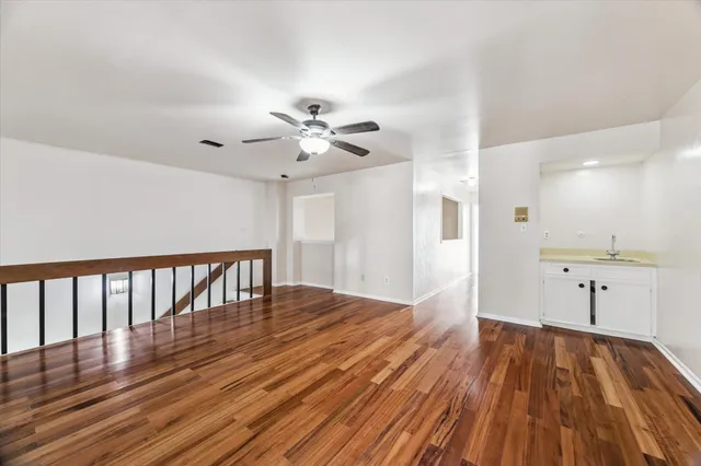 a view of an empty room and kitchen with wooden floor
