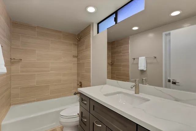 a bathroom with a granite countertop sink a toilet a mirror a bathtub and shower