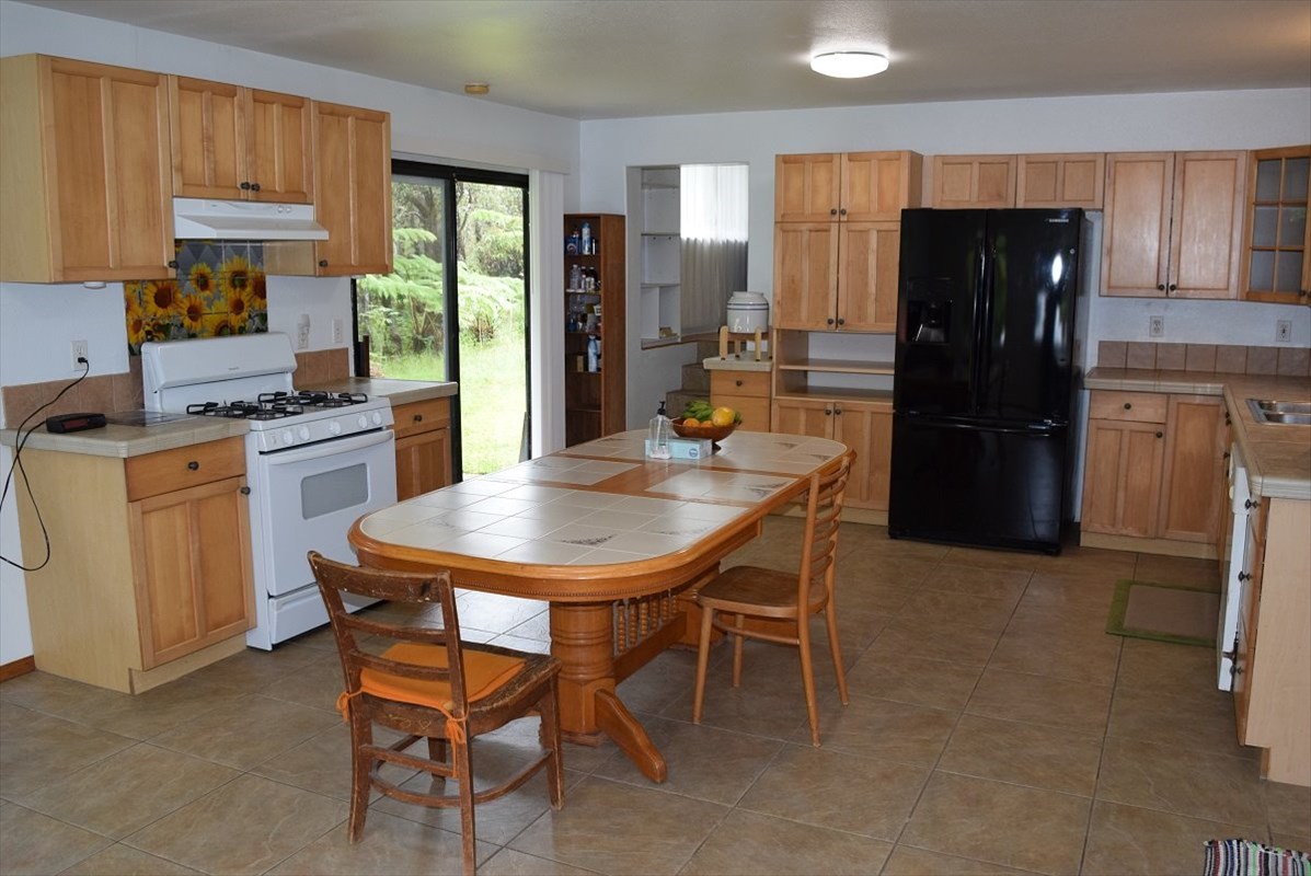 11-2855 Kaleponi Road Mountain View, HI 96771 - Photo 4 of 19 a kitchen with a table chairs refrigerator and cabinets