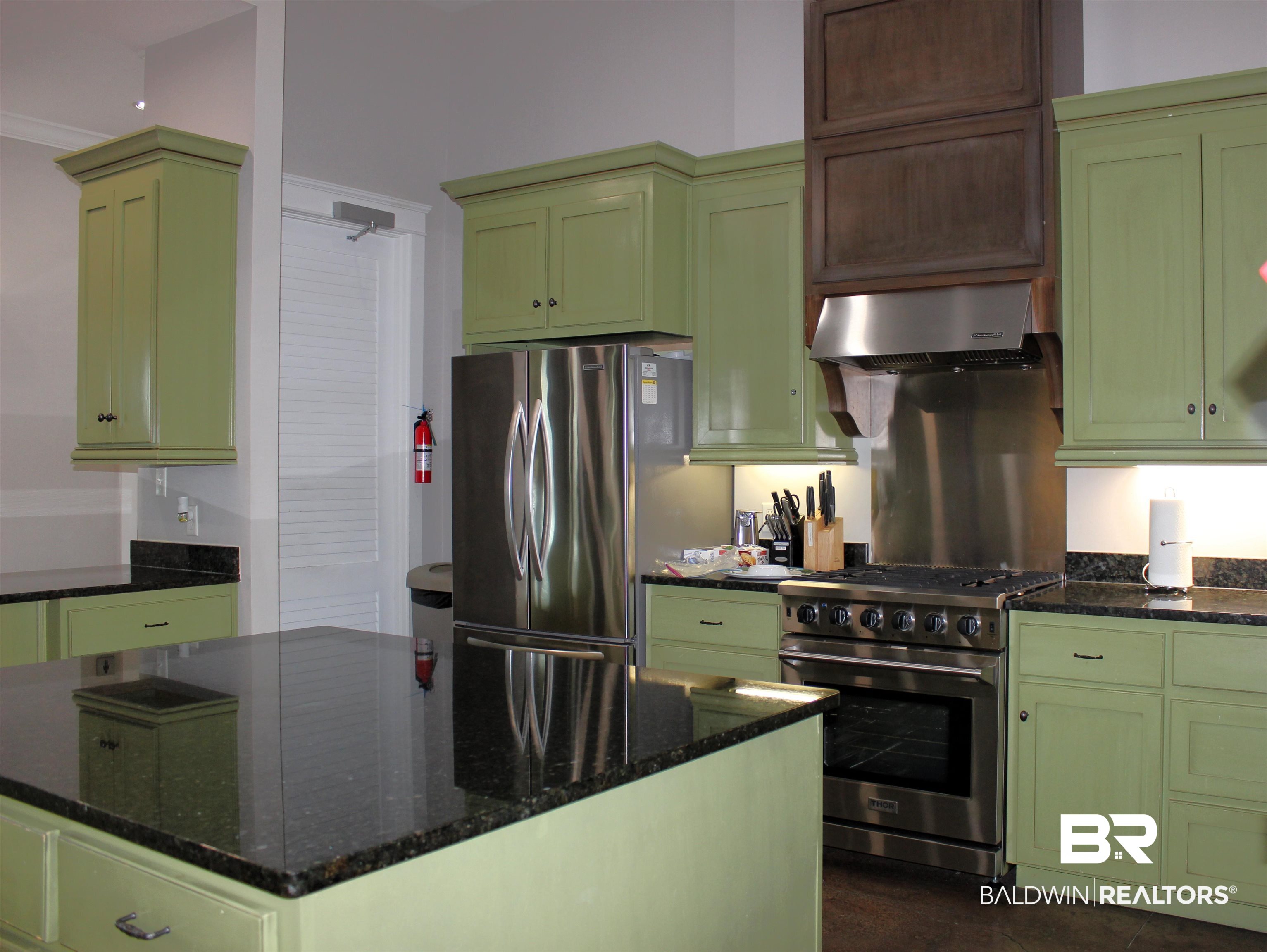11869 Gateway Drive Elberta, AL 36530 - Photo 11 of 78 Kitchen featuring dark stone countertops, green cabinetry, wall chimney exhaust hood, and appliances with stainless steel finishes