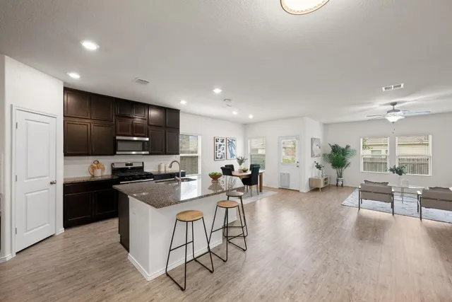 a kitchen with stainless steel appliances kitchen island granite countertop a stove a refrigerator a sink a dining table and chairs with wooden floor