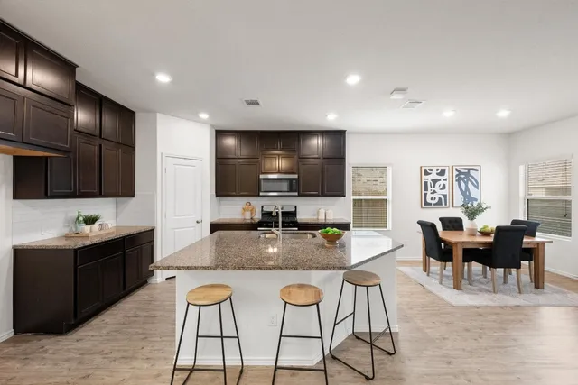 a kitchen with stainless steel appliances granite countertop a stove top oven a sink dishwasher a dining table and chairs with wooden floor