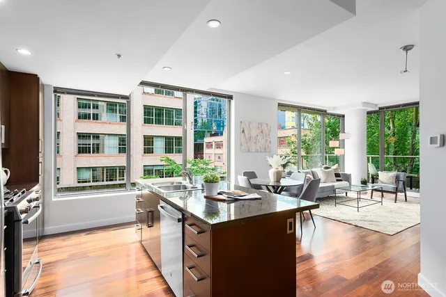 a living room with large windows couches and kitchen view