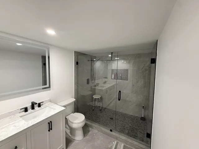 a bathroom with a shower sink vanity mirror and toilet