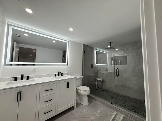 a bathroom with a double vanity sink toilet mirror and shower