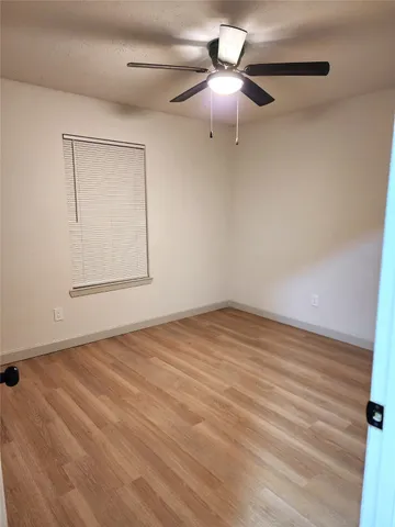 an empty room with wooden floor fan and windows