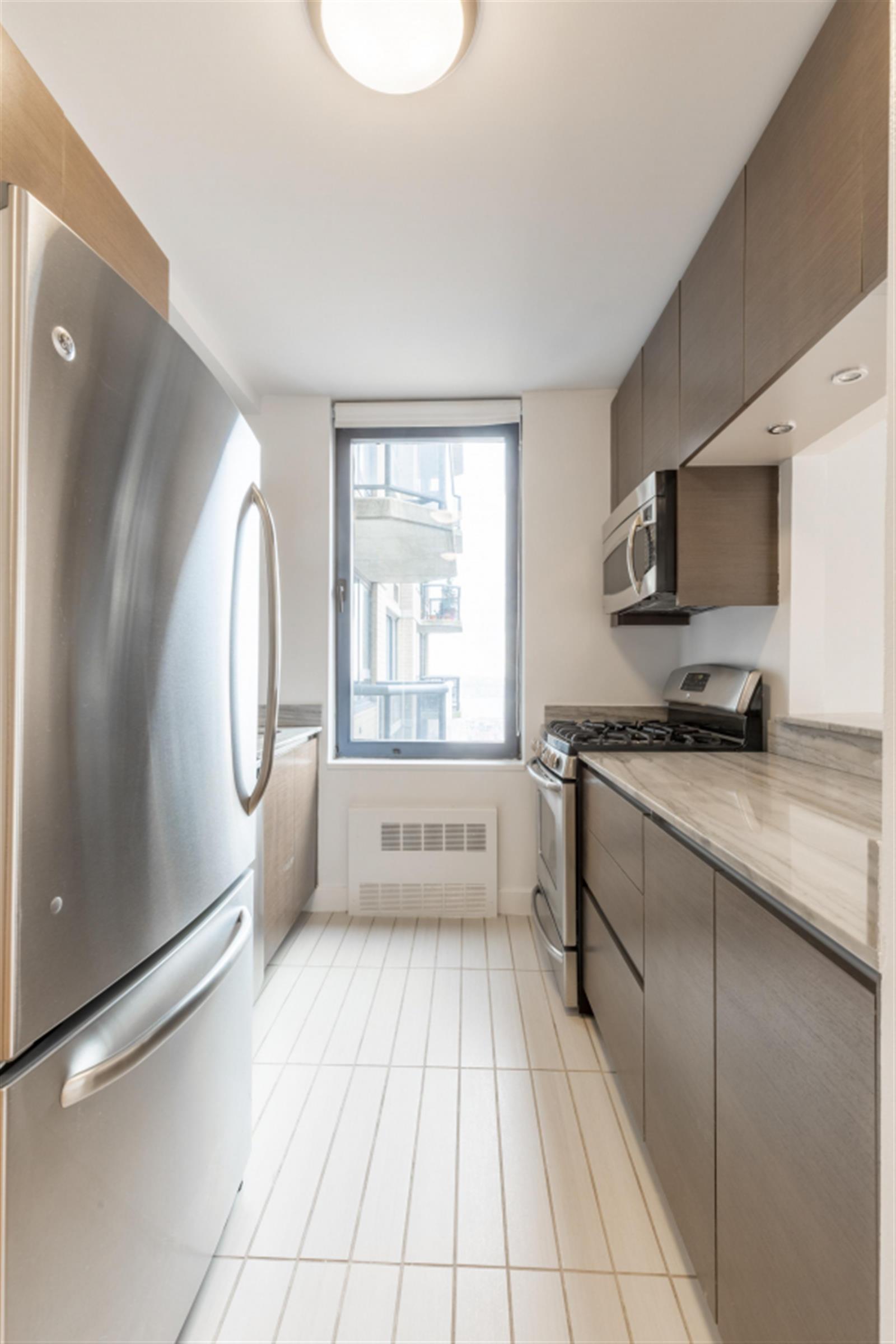 235 West 48th Street, Unit 43M Manhattan, NY 10036 - Photo 4 of 7 a large white kitchen with a sink a microwave and cabinets