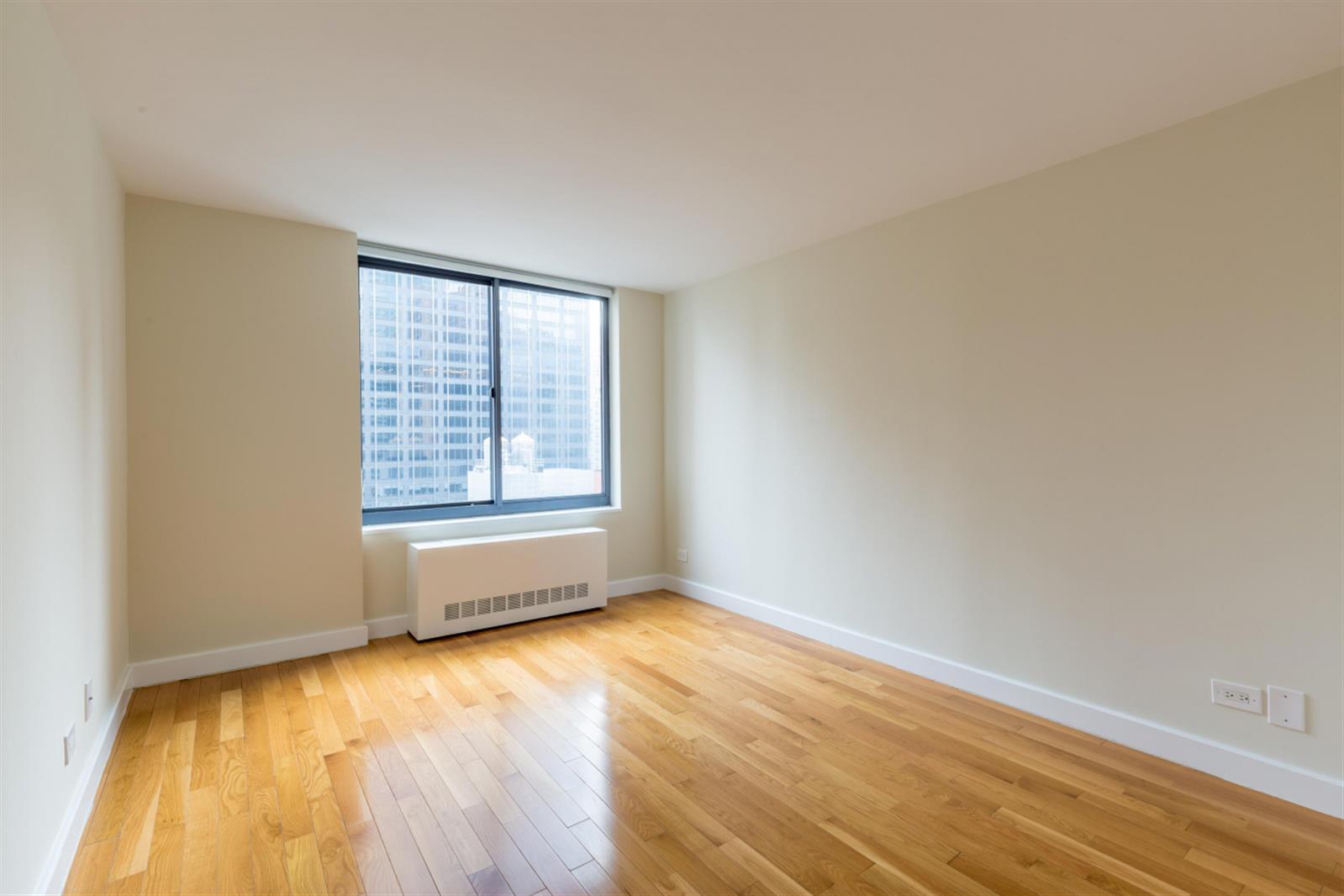 235 West 48th Street, Unit 43M Manhattan, NY 10036 - Photo 5 of 7 a view of an empty room with wooden floor and a window