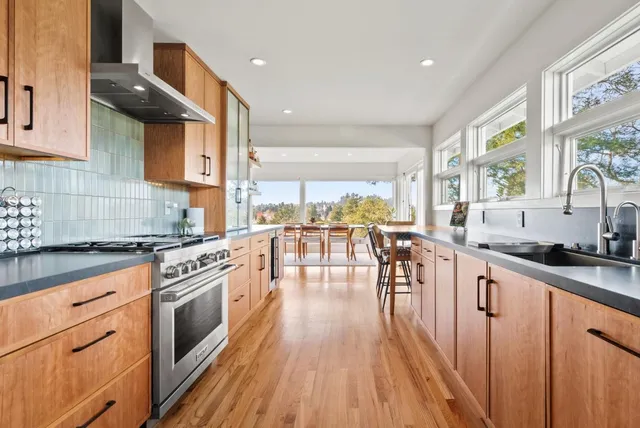 a kitchen with stainless steel appliances granite countertop wooden floors a stove a sink and white cabinets