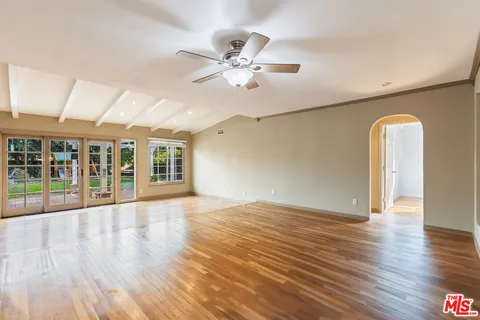 a view of an empty room with wooden floor and a ceiling fan