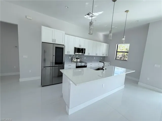 a kitchen with stainless steel appliances granite countertop a refrigerator a sink a stove and white cabinets