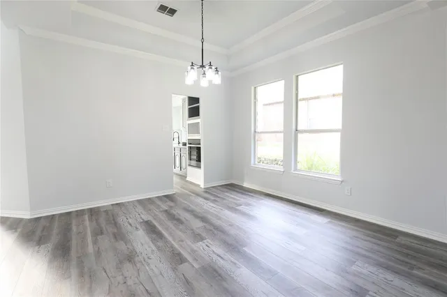 an empty room with wooden floor chandelier and windows