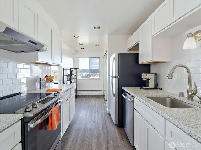 a kitchen with stainless steel appliances a sink dishwasher a refrigerator and a stove with wooden floors