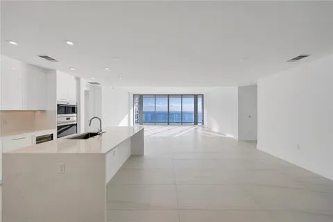 a large white kitchen with kitchen island a sink granite counter tops and a view of living room