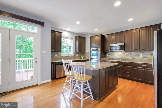 a kitchen with stainless steel appliances granite countertop wooden cabinets a sink a stove a dining table and chairs