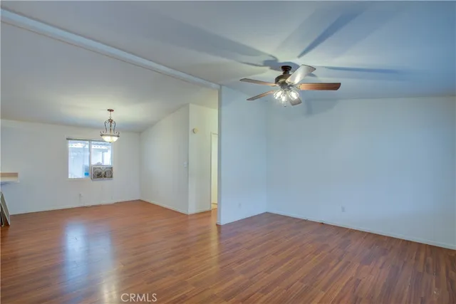 an empty room with wooden floor chandelier fan and windows