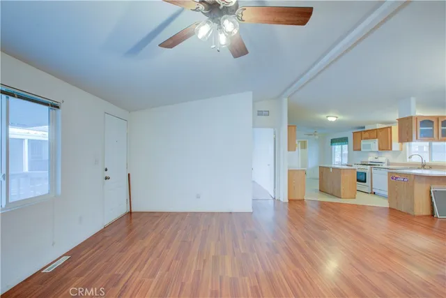 a view of an empty room and kitchen with wooden floor