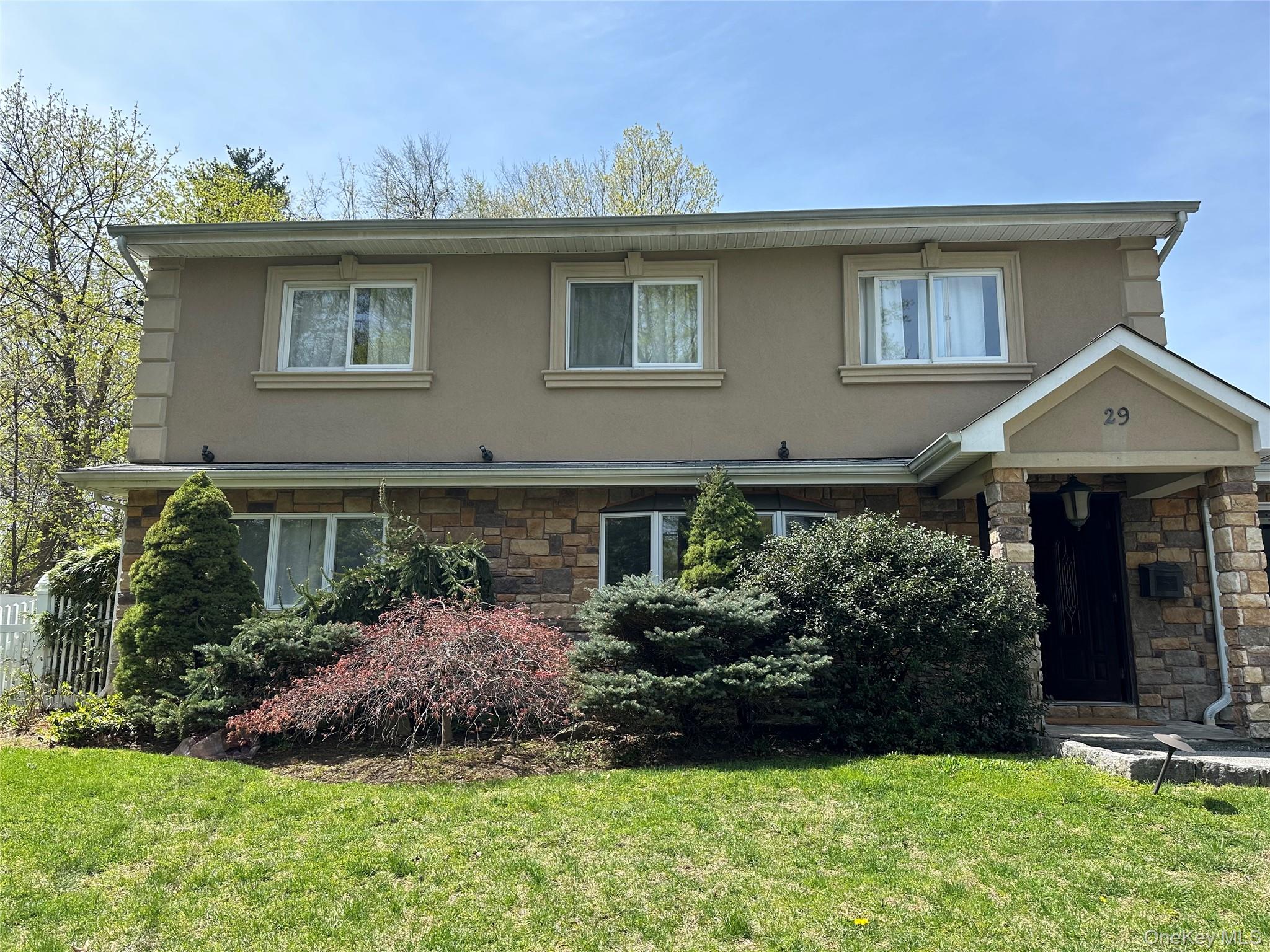 View of front of property with stone siding, stucco siding, and a front lawn