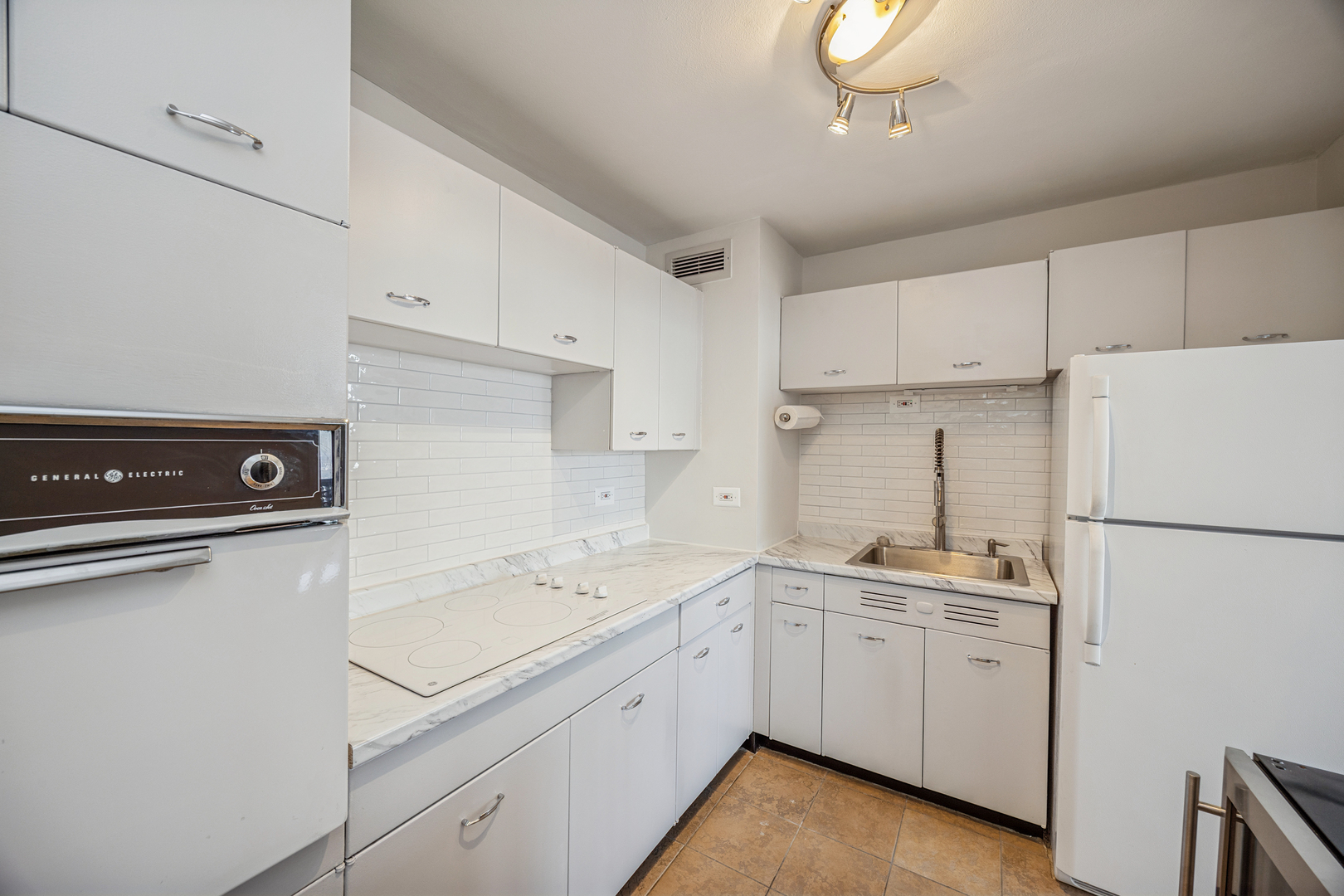 6301 North Sheridan Road, Unit 23J Chicago, IL 60660 - Photo 11 of 21 a kitchen with a sink a stove a refrigerator and white cabinets