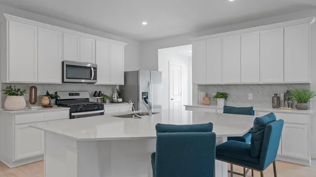 a kitchen with stainless steel appliances a stove a sink a refrigerator white cabinets and a chairs