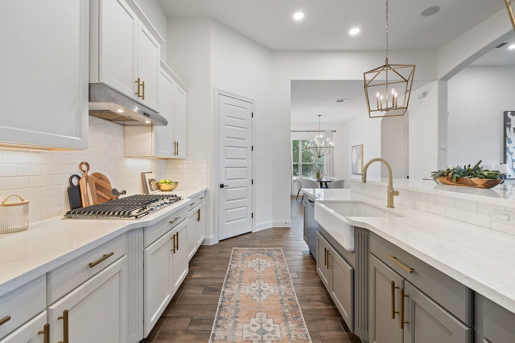 17641 Stratus Cove Dripping Springs, TX 78620 - Photo 10 of 40 Two tone kitchen featuring light stone countertops, dark wood finished floors, dual tone cabinets, tasteful backsplash, and a chandelier