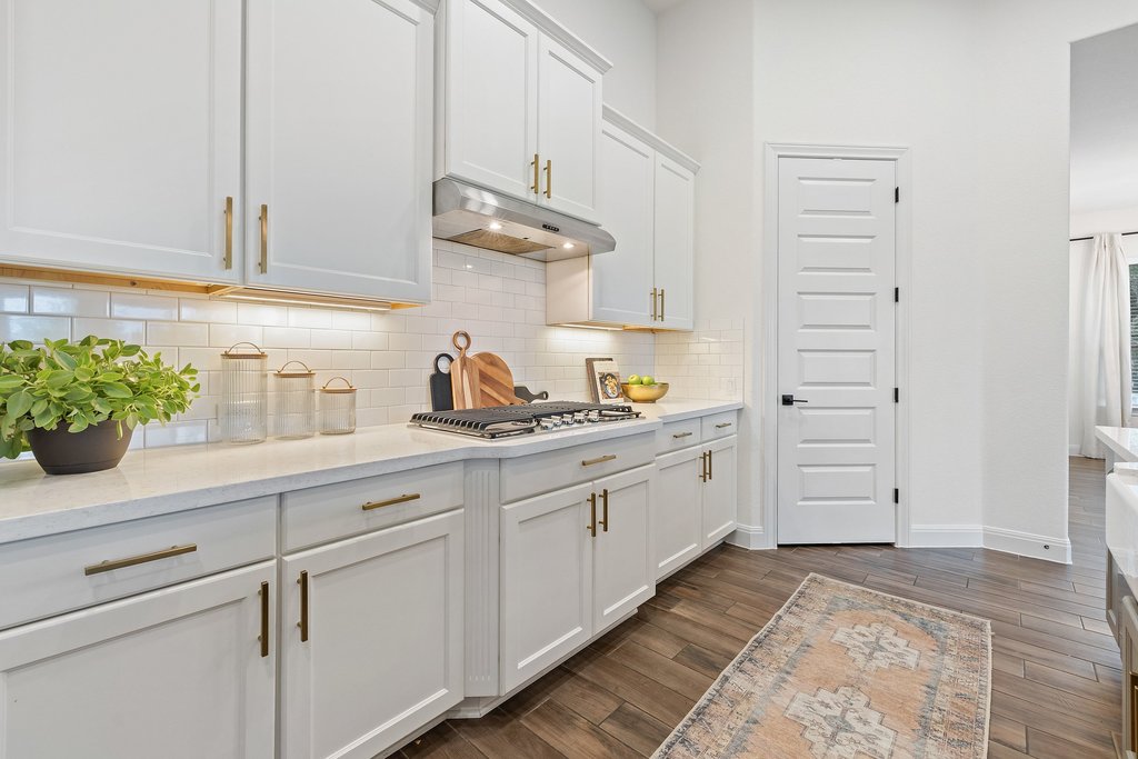17641 Stratus Cove Dripping Springs, TX 78620 - Photo 11 of 40 Kitchen featuring white cabinetry, dark wood-style flooring, light stone countertops, decorative backsplash, and stainless steel gas cooktop