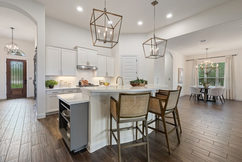17641 Stratus Cove Dripping Springs, TX 78620 - Photo 13 of 40 Dual tone kitchen featuring hanging lights, arched walkways, a kitchen breakfast bar, a kitchen island with sink, and wood tiled floors