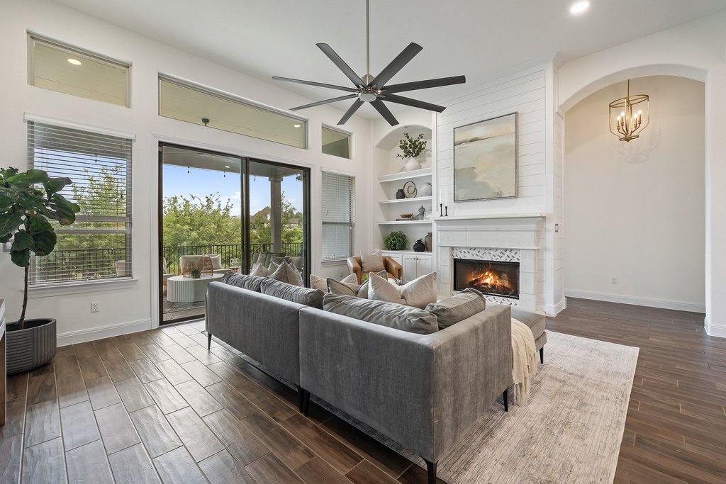 17641 Stratus Cove Dripping Springs, TX 78620 - Photo 16 of 40 Living room featuring built in features, a ceiling fan, wood tiled floors, a lit fireplace, and arched walkways