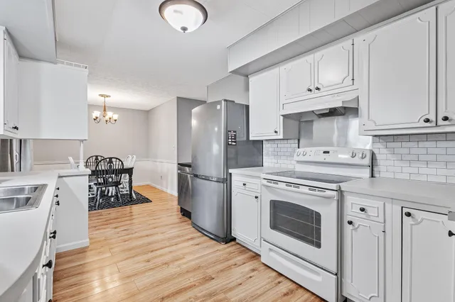 a kitchen with stainless steel appliances granite countertop a stove a sink dishwasher and a refrigerator with white cabinets