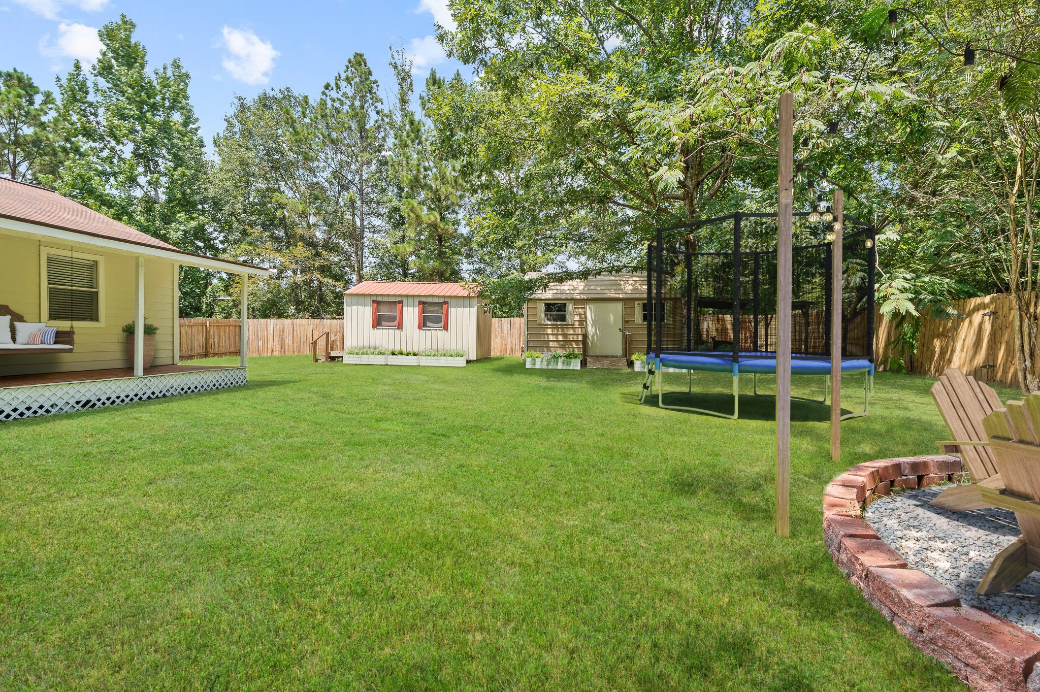 61 Hicks Loop West Cleveland, TX 77328 - Photo 36 of 38 Expansive backyard oasis featuring lush green lawn, cozy wooden deck, storage sheds, and a trampoline, perfect for family fun and relaxation.