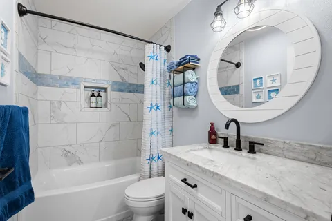 a bathroom with a granite countertop bathtub sink vanity mirror and toilet