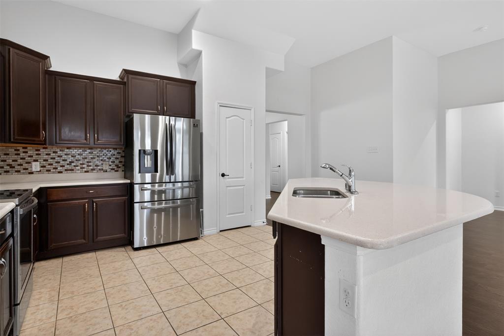 8728 Maple Ridge Trail Fort Worth, TX 76244 - Photo 16 of 40 Kitchen featuring an island with an undermount sink, stainless steel appliances, dark wood cabinetry, a mosaic tile backsplash, and light tile flooring