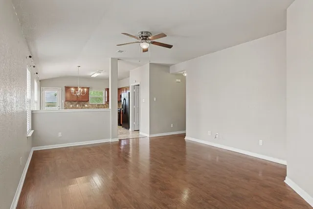 a view of an empty room with wooden floor and a ceiling fan