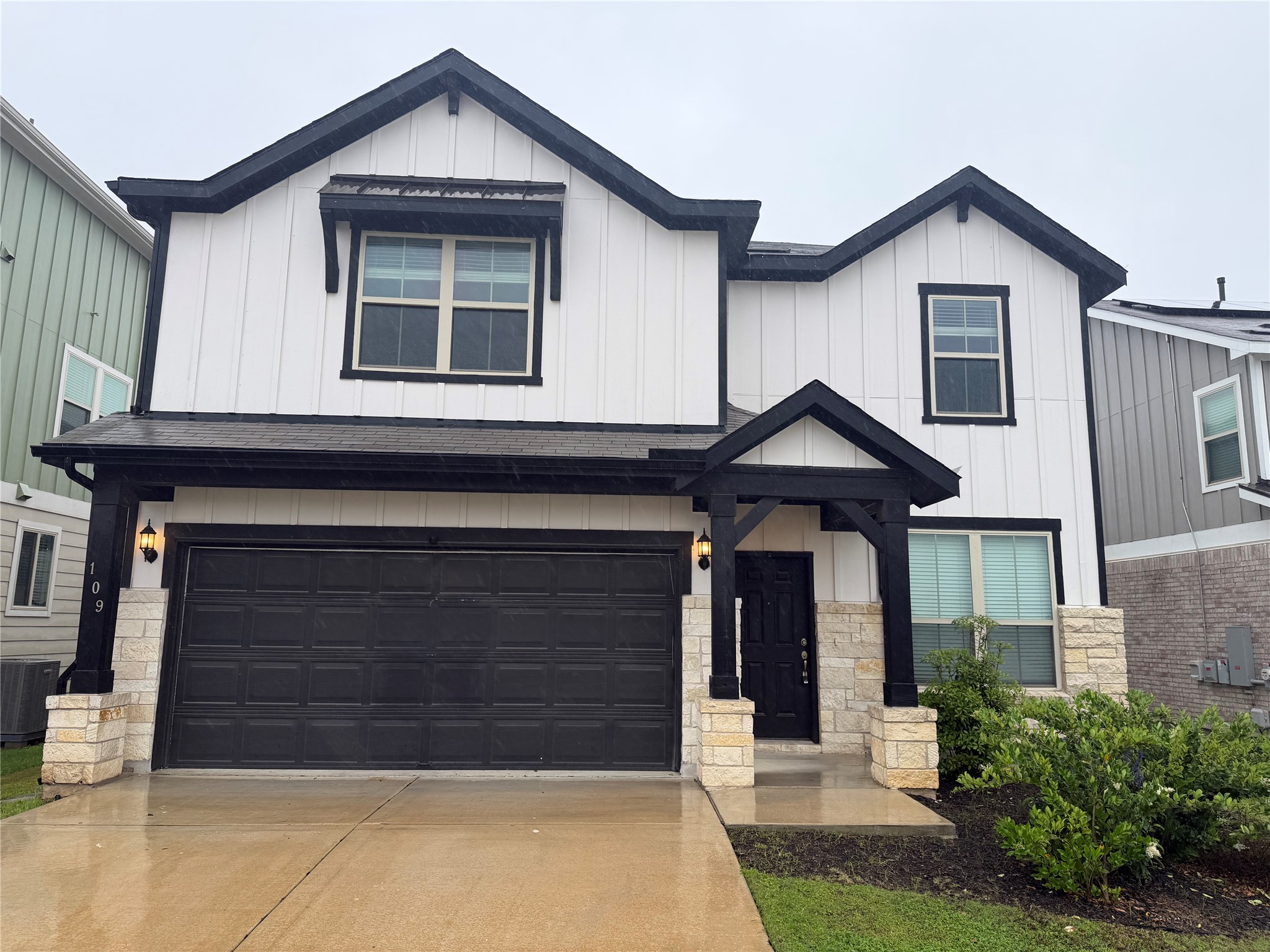 Modern farmhouse exterior featuring white vertical siding, black trim, a covered entry, an attached garage, and stone veneer accents